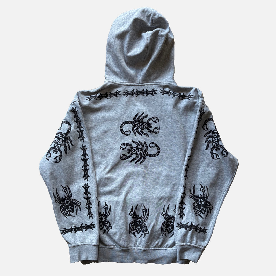 A light gray heather hoodie shown from the back, featuring black graphic prints of scorpions and barbed wire along the shoulders, sleeves, and lower back, laid flat against a light gray background.