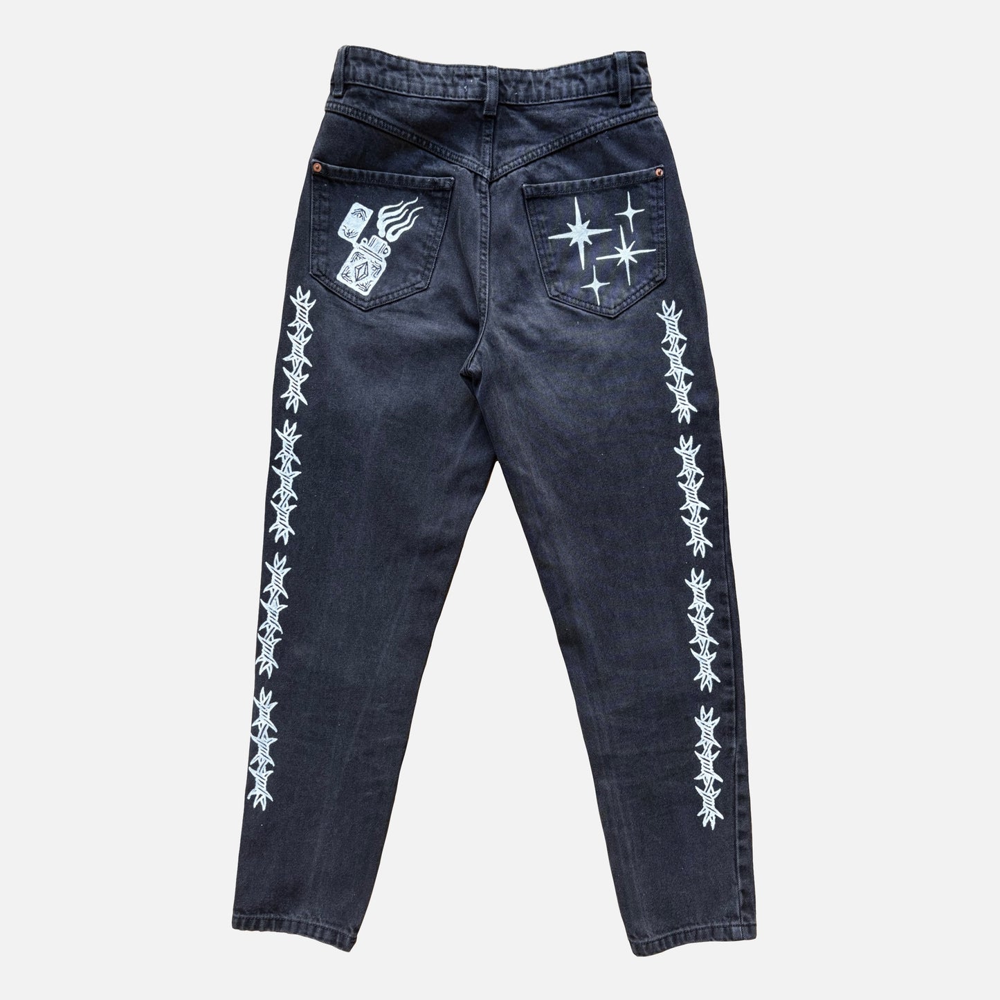 Dark washed denim jeans shown from the back, featuring white printed barbed wire patterns down both legs and white graphic designs on the back pockets.