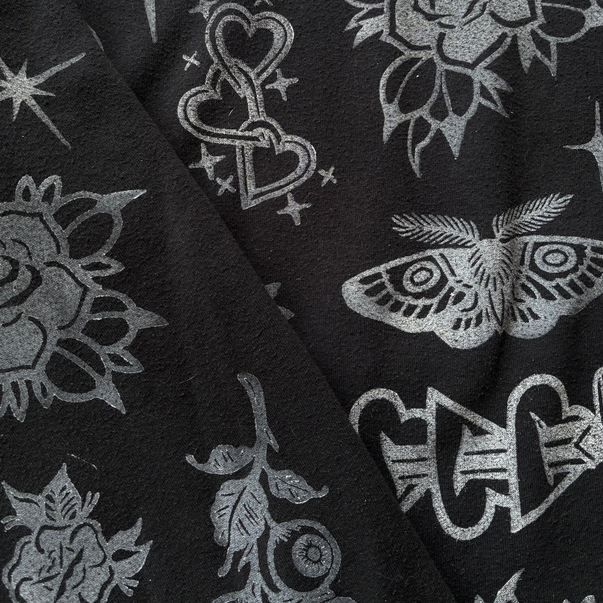 Close-up of a black fabric with a white print featuring roses, moths, stars, and interlocking hearts.