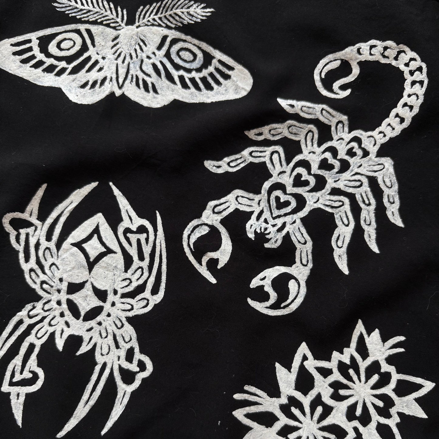 Black fabric featuring white or printed motifs including a moth, scorpion, barbed wire border.