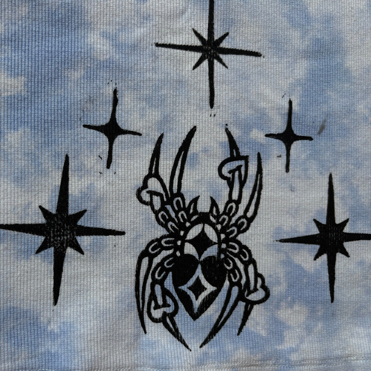 Close-up of a light blue and white tie-dye fabric featuring black printed spider and starburst motifs.