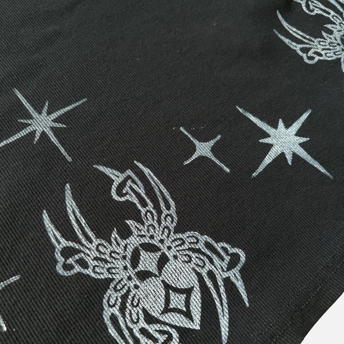Close-up of a black babydoll dress surface with a repeating white printed star and spider pattern.