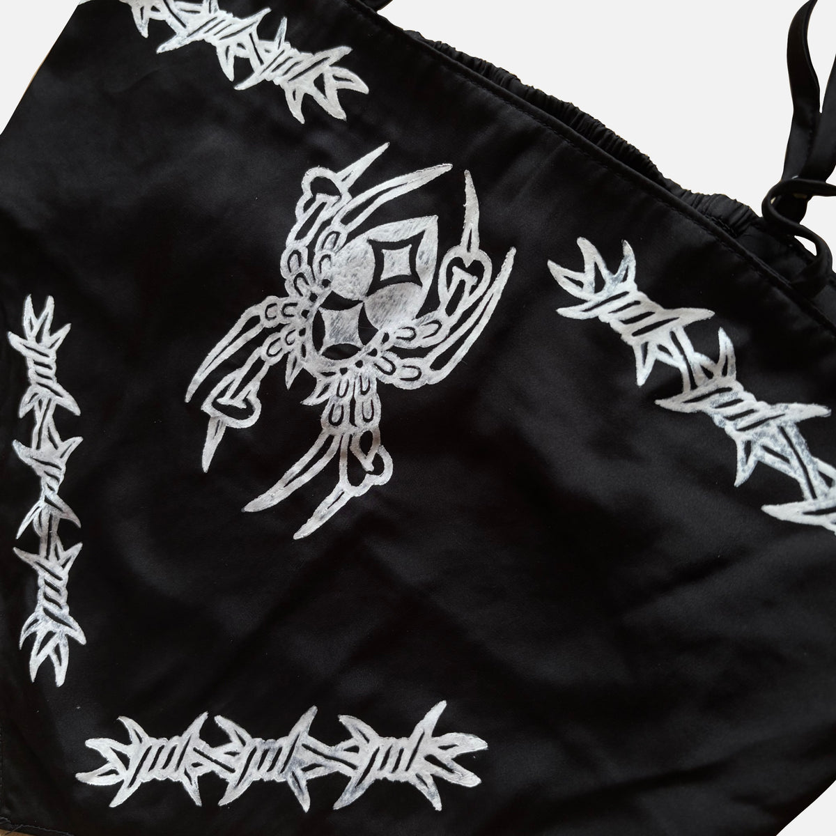 Black fabric crop top with white printed gothic-style designs, including a central ornate spider and barbed border motifs, shown in a close-up studio shot.