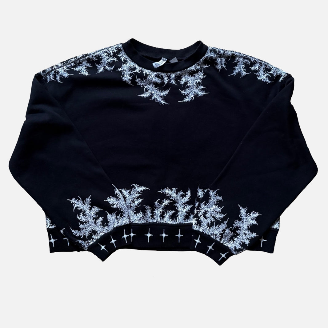 A black cropped crewneck sweater with intricate white painted patterns along the shoulders, neckline, hem, and across the front.
