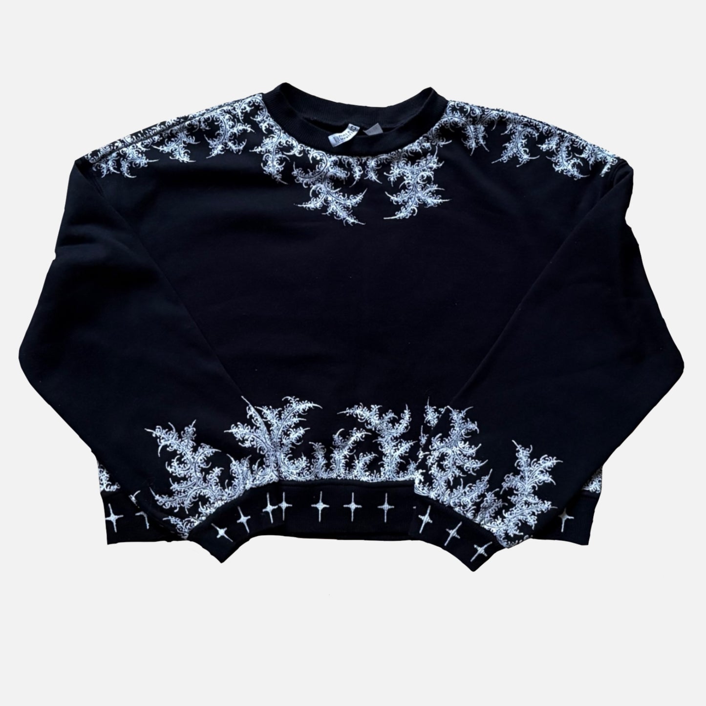 A black cropped crewneck sweater with intricate white painted patterns along the shoulders, neckline, hem, and across the front.