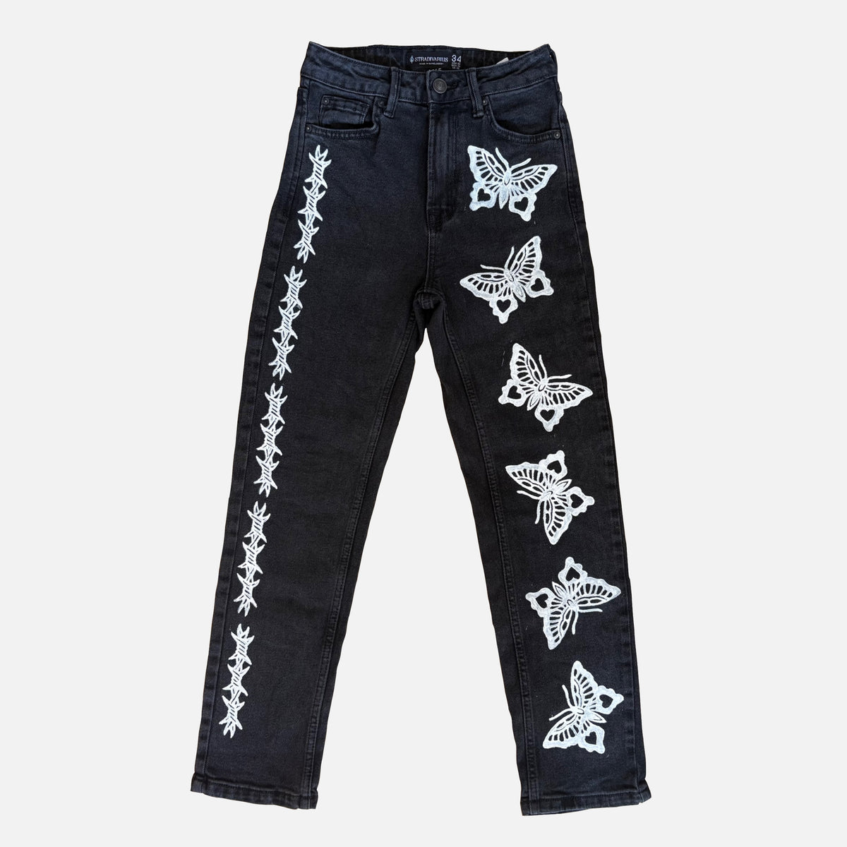 Black denim jeans featuring white printed butterfly and barbed wire patterns running down both legs, displayed flat against a light gray background.