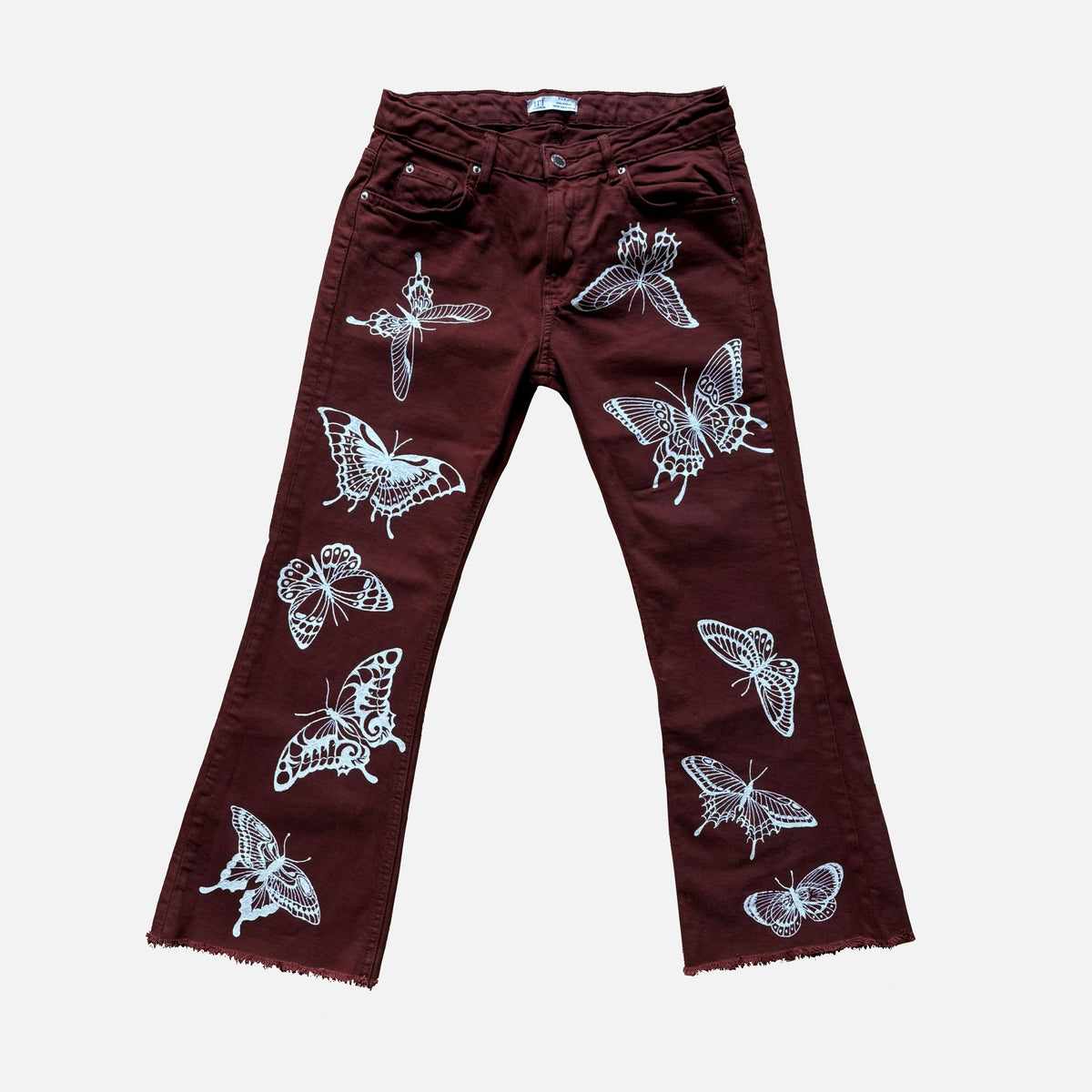 A pair of dark burgundy flare jeans with white painted butterfly and moth patterns, shown flat against a light gray background.