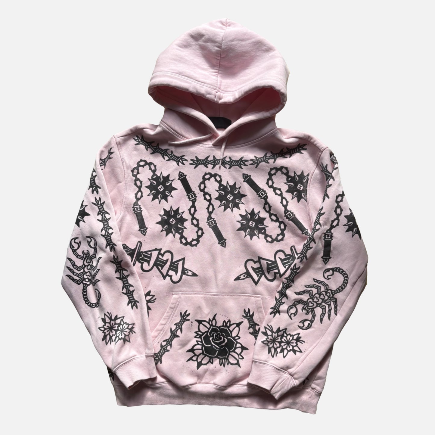 A light pink pullover hoodie featuring black gothic-style graphic prints of scorpions, chains, roses, and barbed wire designs, displayed against a light gray background.
