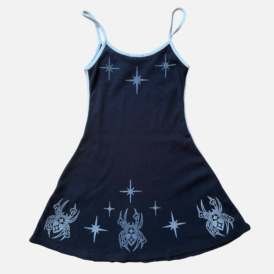 A black sleeveless dress with white spaghetti straps and printed white star and spider motifs on a light gray background.