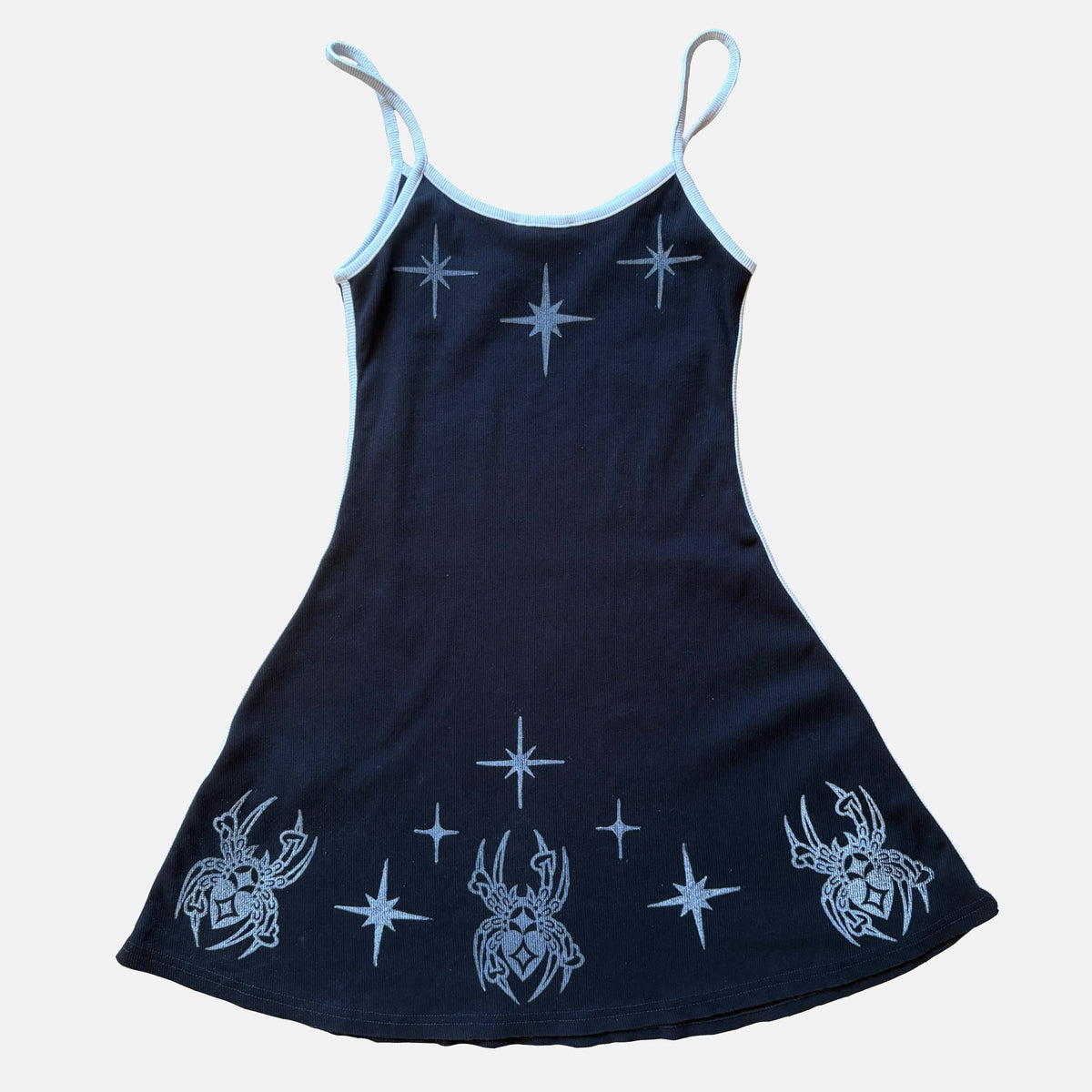 A black sleeveless dress with white spaghetti straps and printed white star and spider motifs on a light gray background.