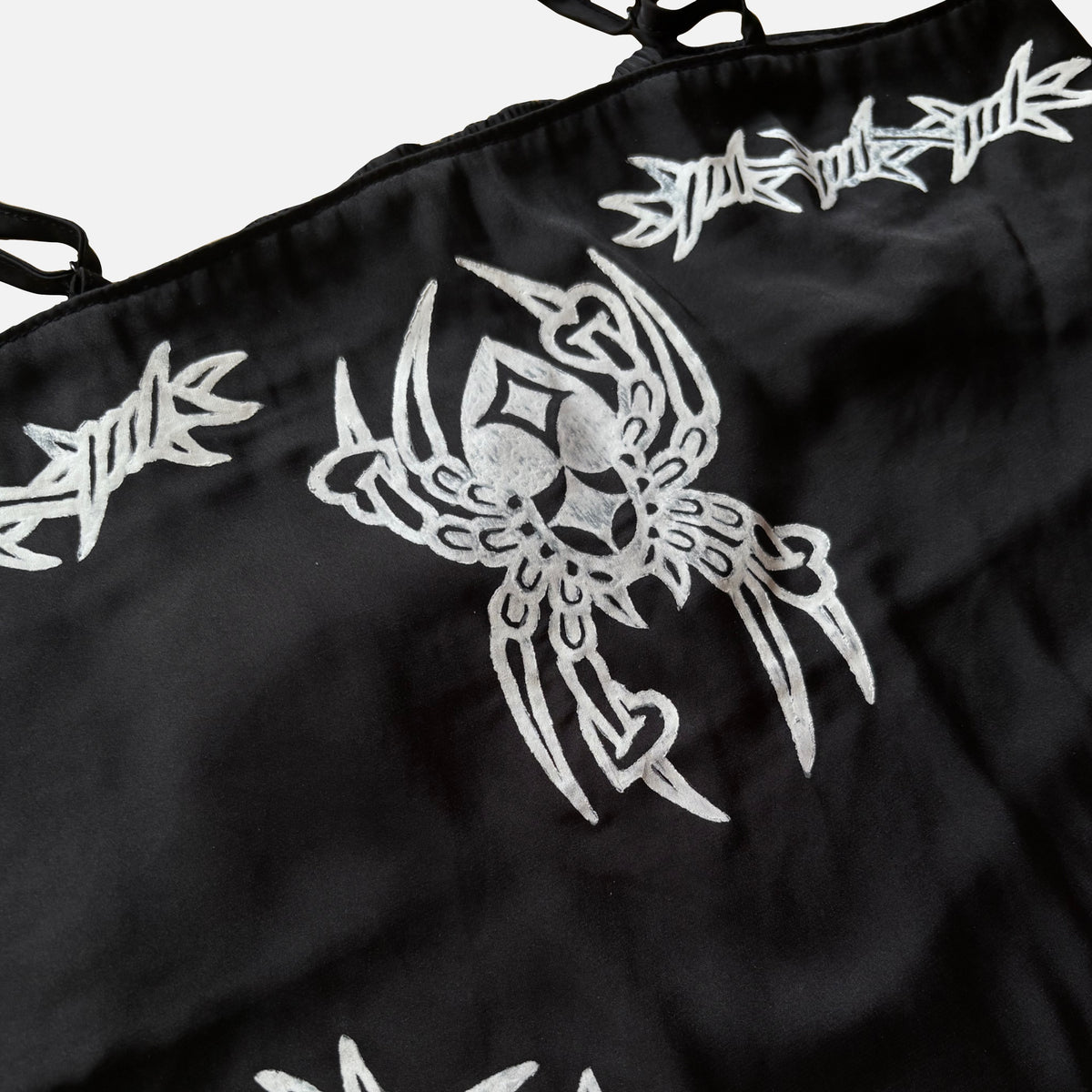 Close-up of a black fabric item, featuring white embroidered barbed wire and a large stylized spider graphic.