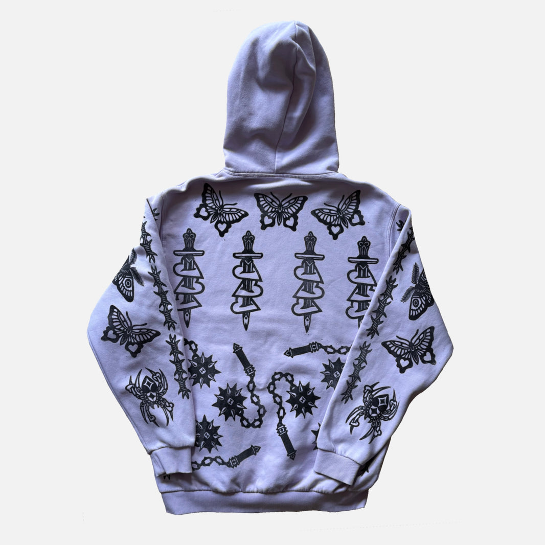 A light lavender-gray pullover hoodie shown from the back, featuring a black graphic print of butterflies, daggers, chains, and spiders.