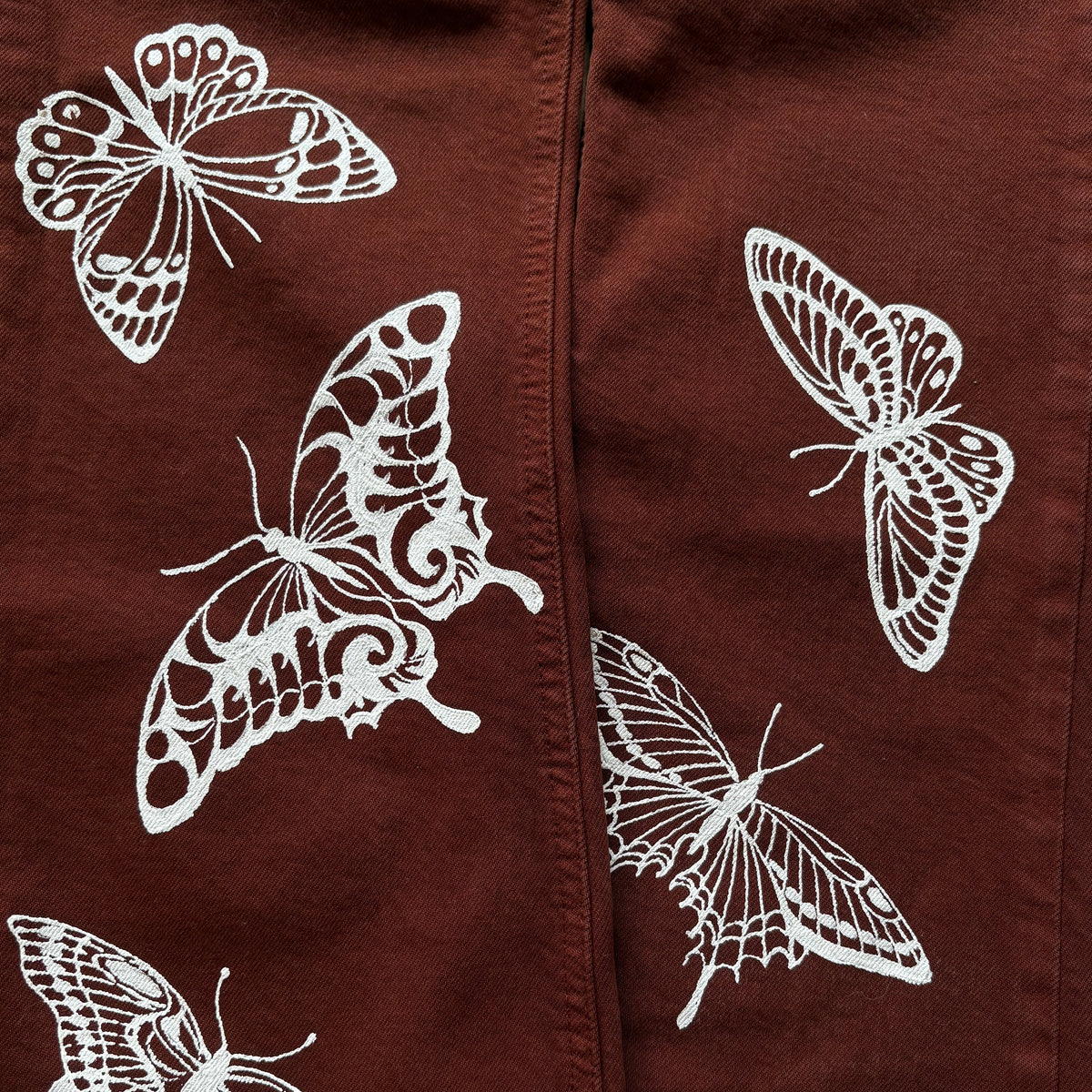 A close-up of a dark brown garment featuring a white printed pattern of butterflies and moths