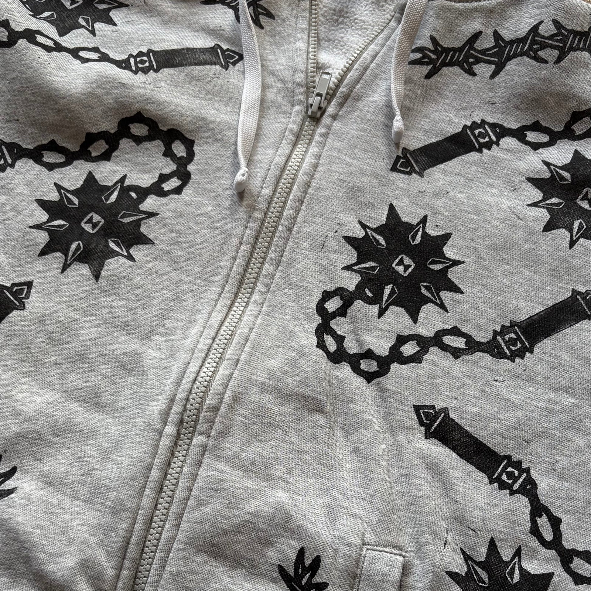 A light gray heather zip-up hoodie featuring a black graphic print of flails laid flat on a light surface.