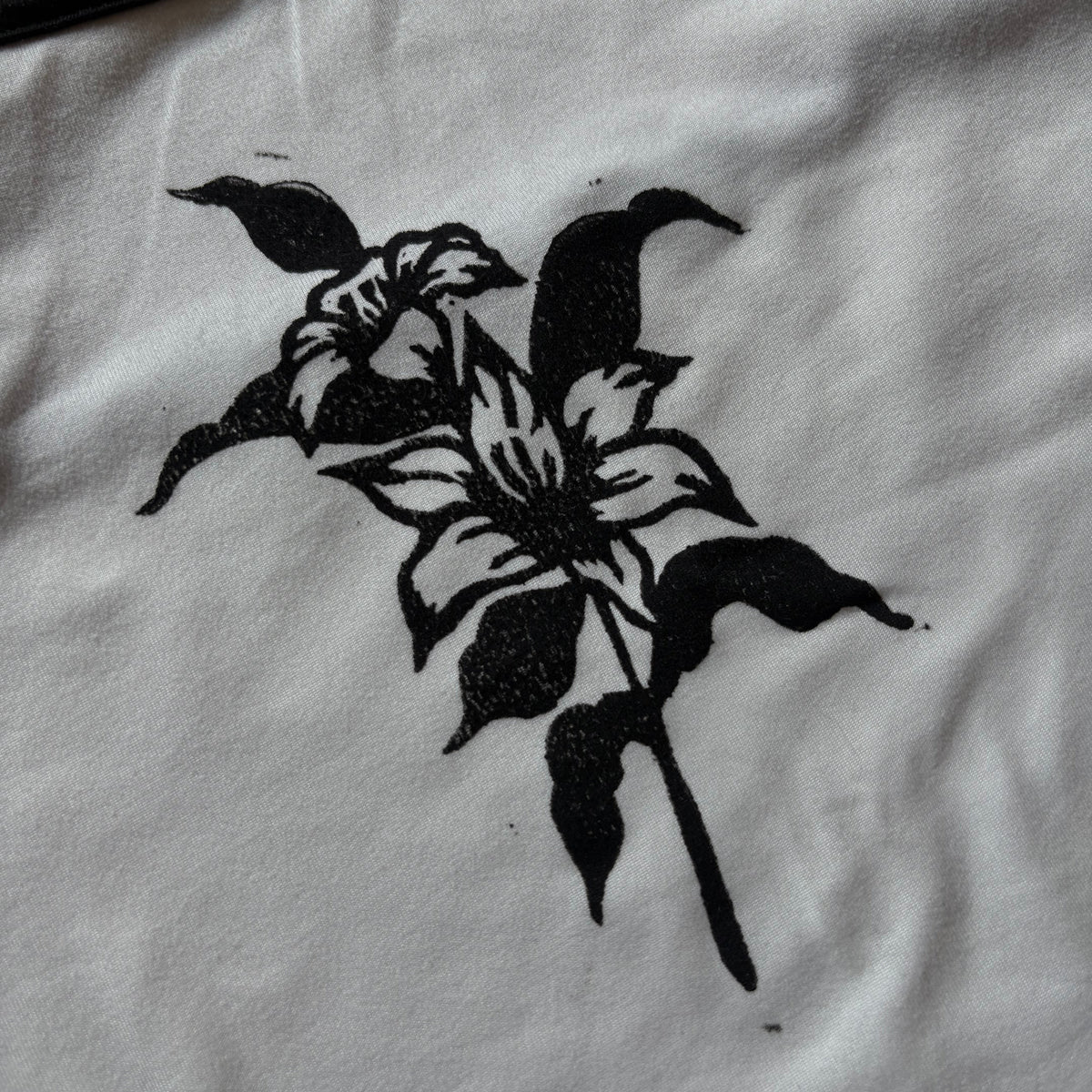 A close-up of a white fabric surface featuring a black stenciled or printed floral motif, with part of a dark trim visible along the top edge.