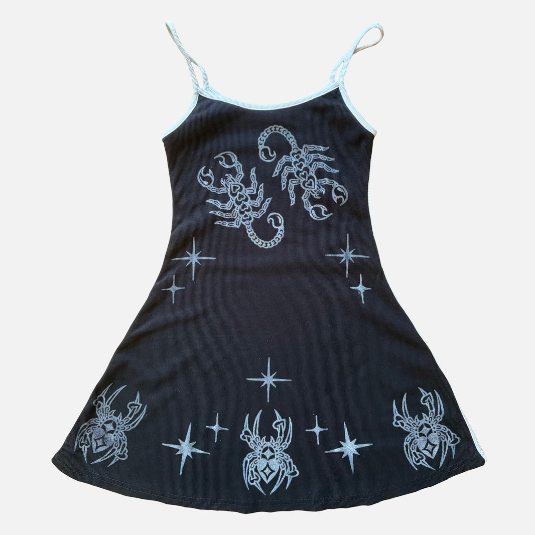 A black spaghetti-strap babydoll dress featuring white celestial prints of spiders, scorpions, and stars, displayed flat against a light gray background.