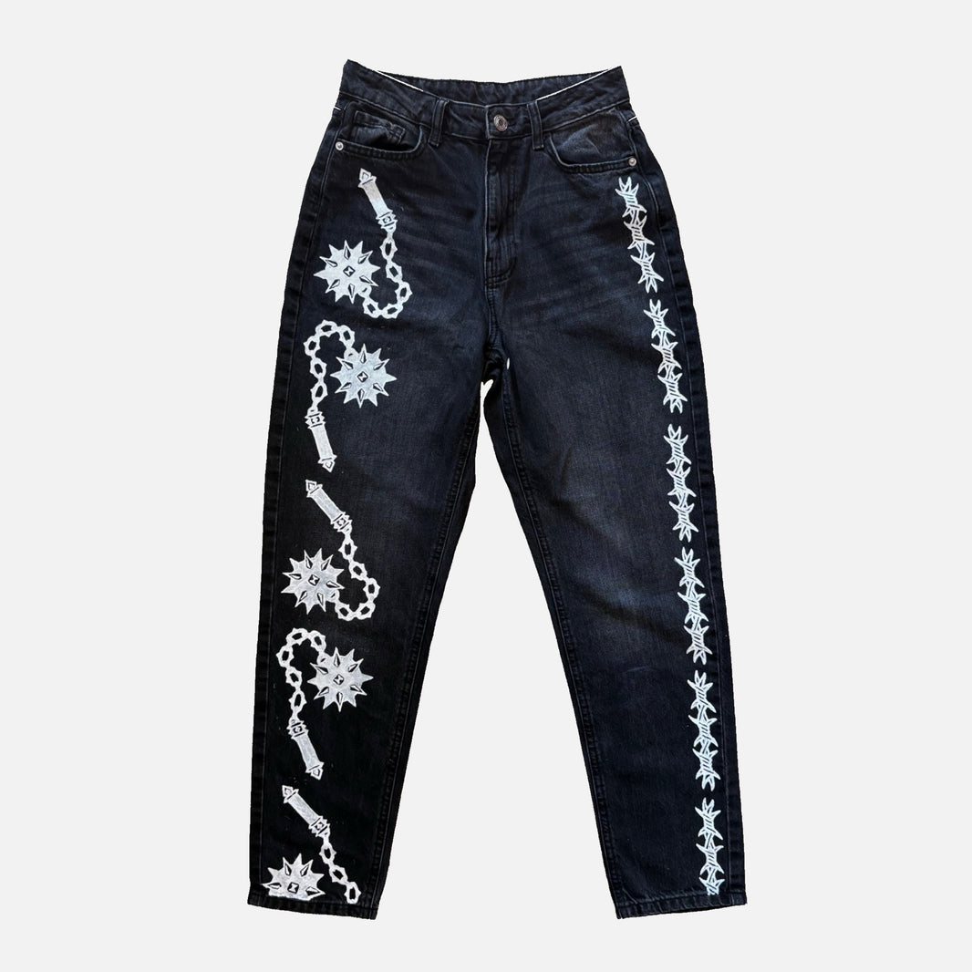 Dark wash denim jeans featuring white printed flail and barbed wire motifs running down both legs, displayed flat against a light gray background.