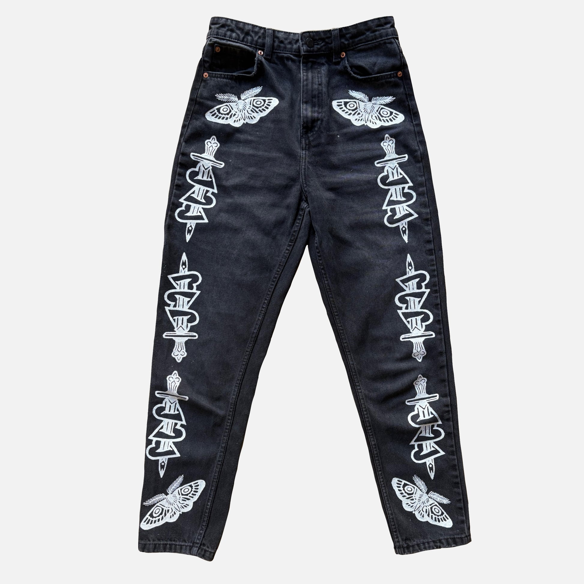 Black denim jeans featuring white printed motifs of moths and stacked knives down the outer thighs, displayed flat against a light gray background.