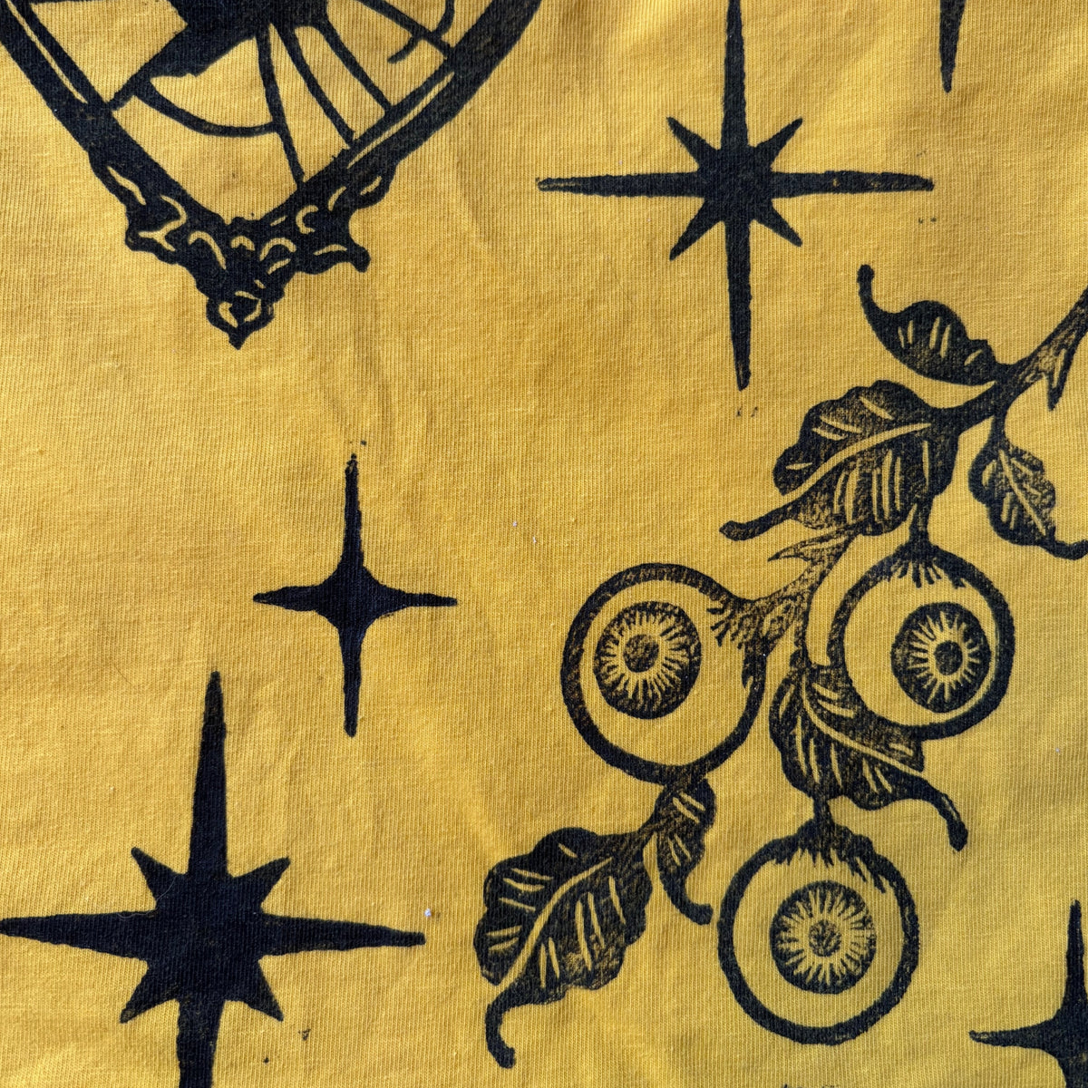A close-up of a yellow crop top printed with black botanical and celestial motifs, including starbursts and a leafy branch with round fruit.