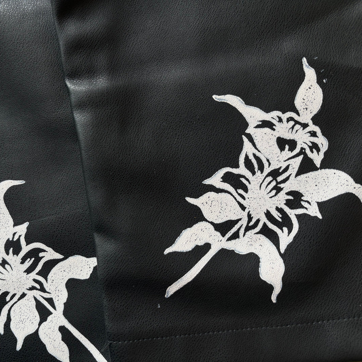 Close-up of a black leather or faux-leather surface with two white floral cutout or printed motifs.