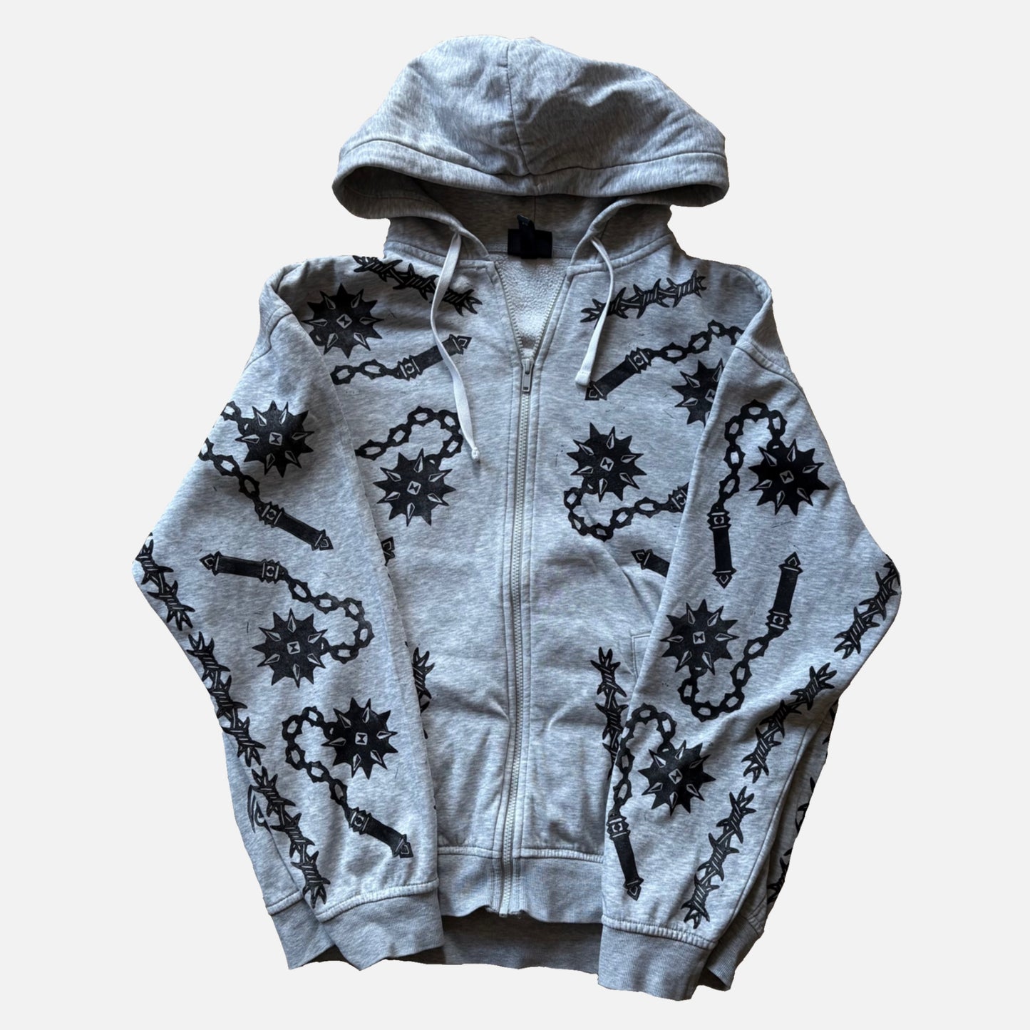 A light gray zip-up hoodie featuring a black graphic print of flails and barbed wire motifs, laid flat against a light gray background.