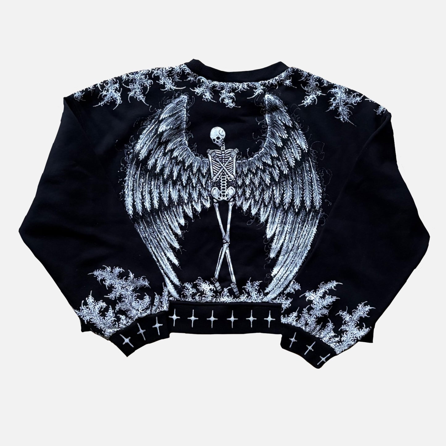 A black cropped sweatshirt featuring a large white graphic of a winged skeleton centered on the back, with printed white details along the shoulders, cuffs, and hem.