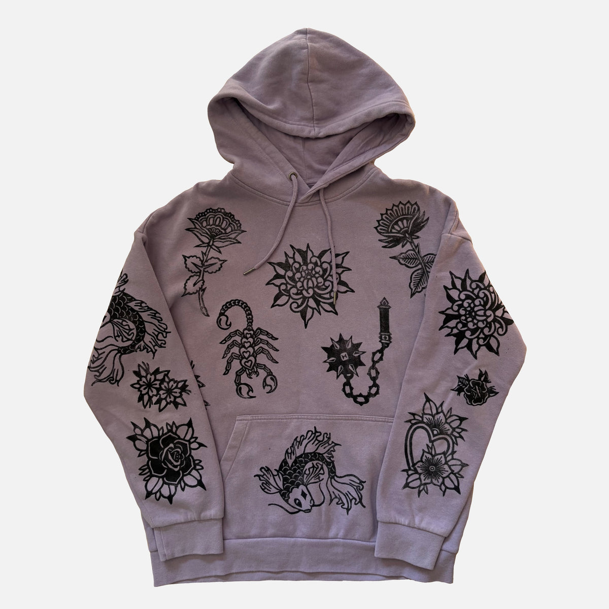 A light purple/lavender pullover hoodie featuring black line art illustrations of flowers, a scorpion, a koi fish, and a heart, displayed against a light gray background.
