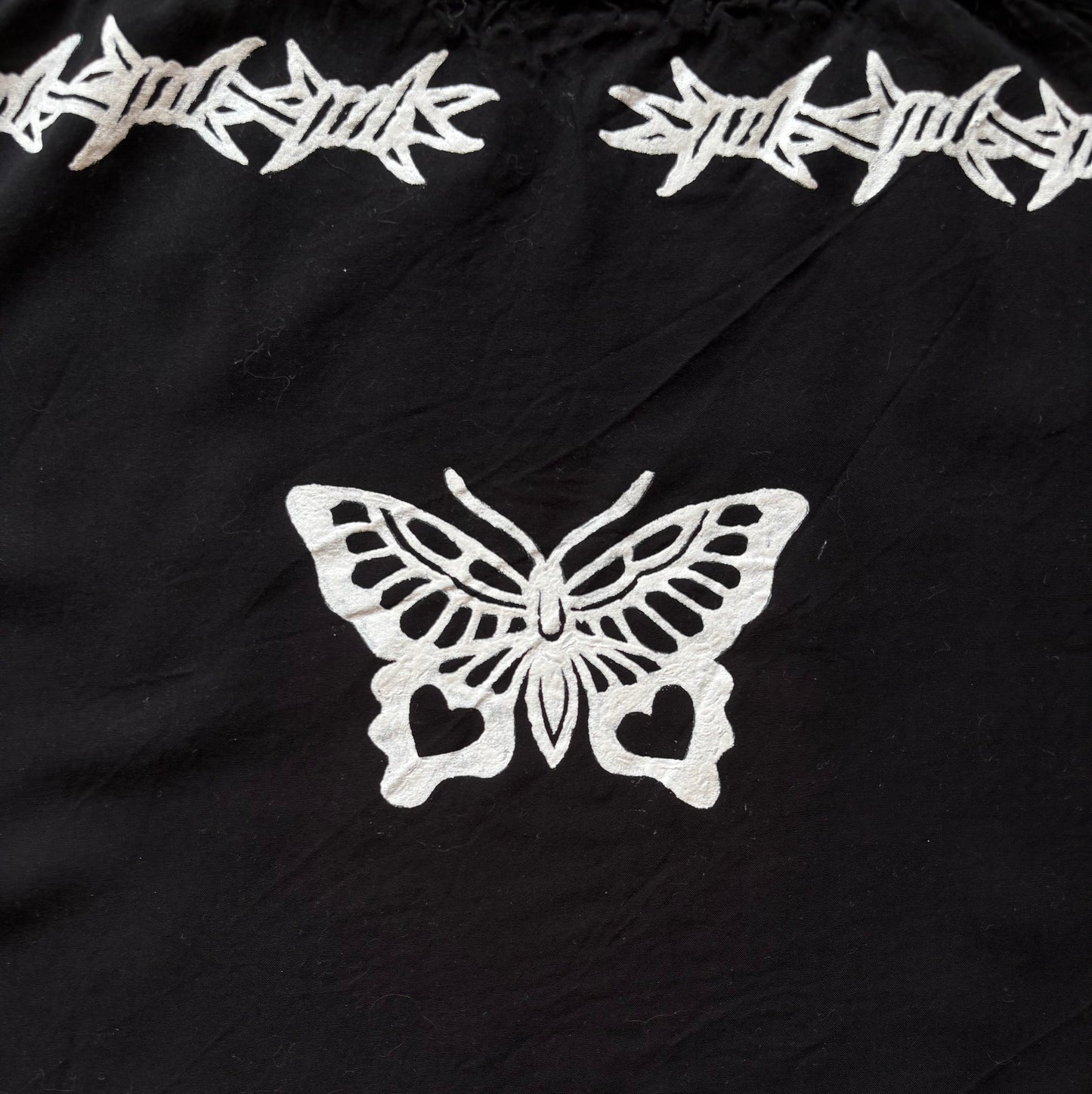 Black fabric with white printed barbed wire motifs along the top and bottom edges and a large white butterfly motif in the center.