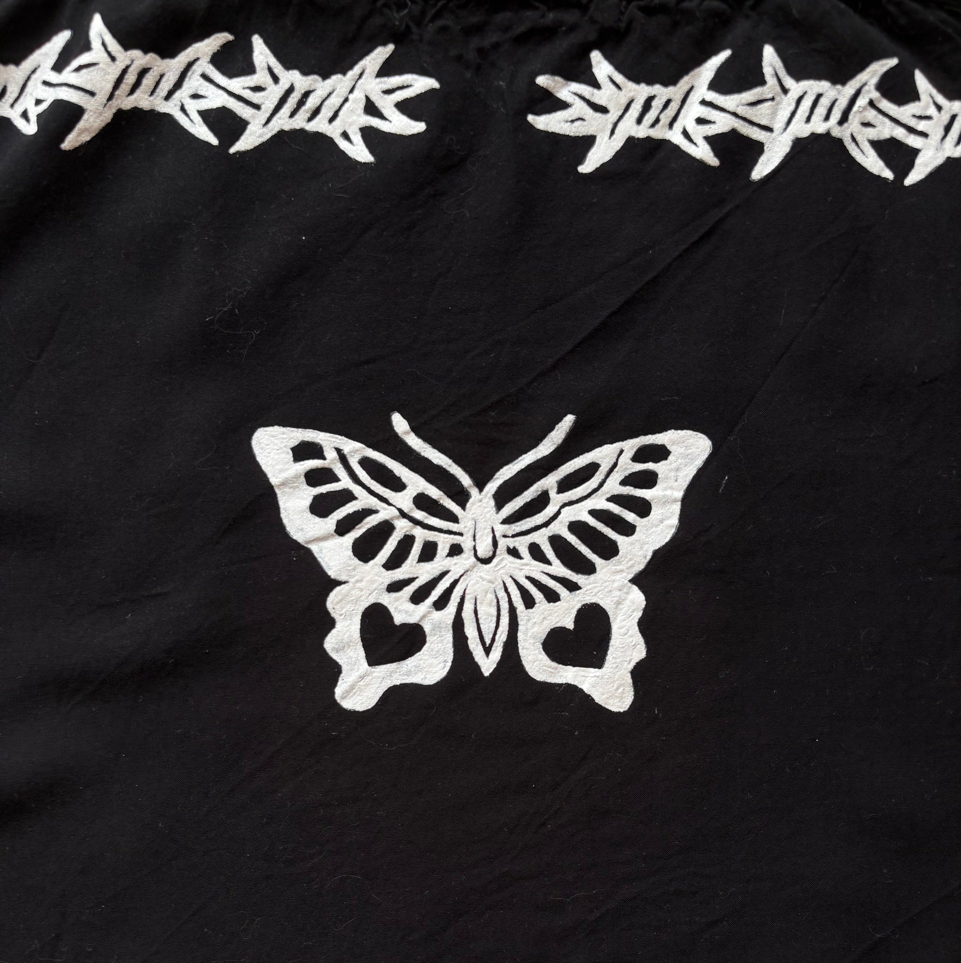 Black fabric with white printed barbed wire motifs along the top and bottom edges and a large white butterfly motif in the center.