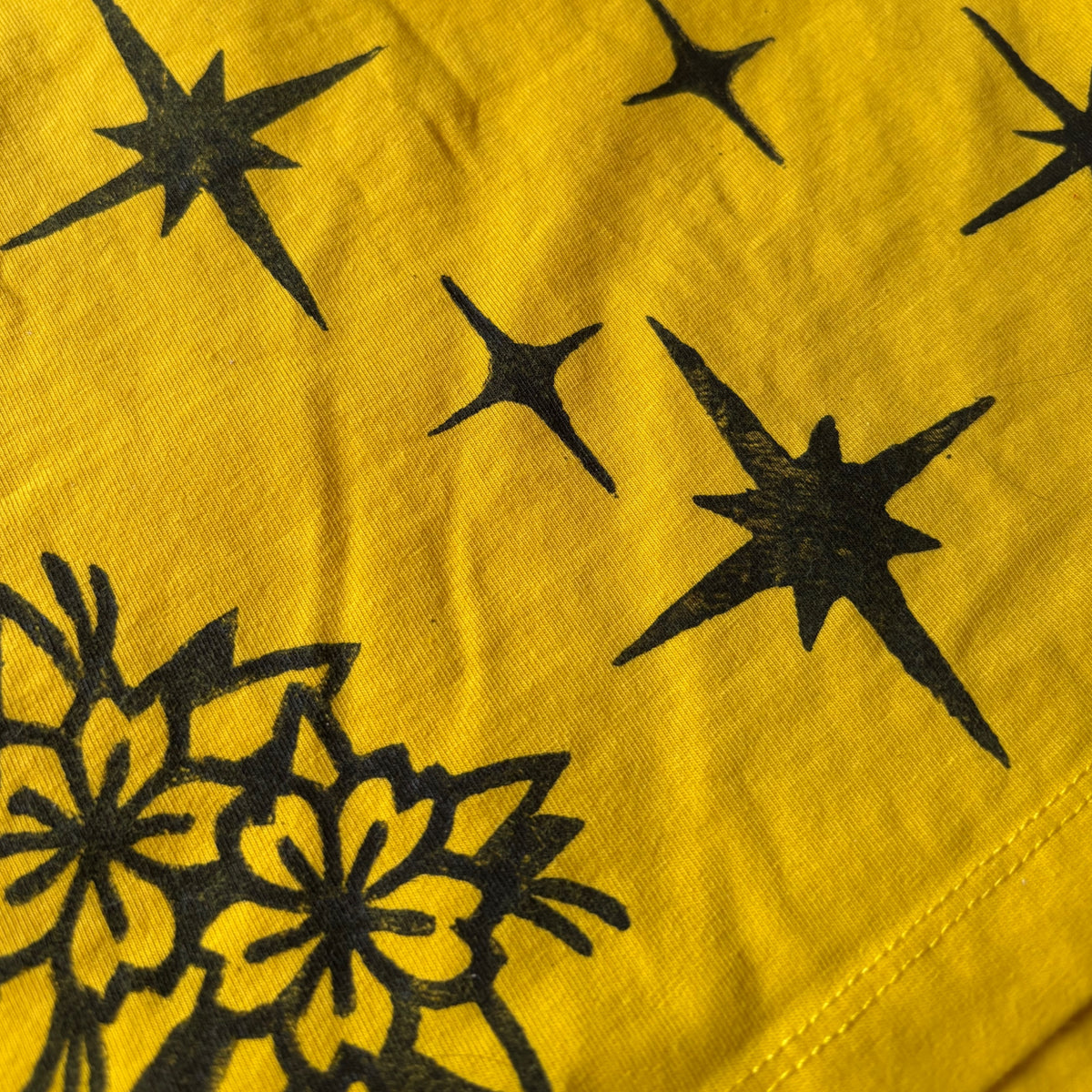 Close-up of a yellow crop top surface with black starburst and floral printed motifs.