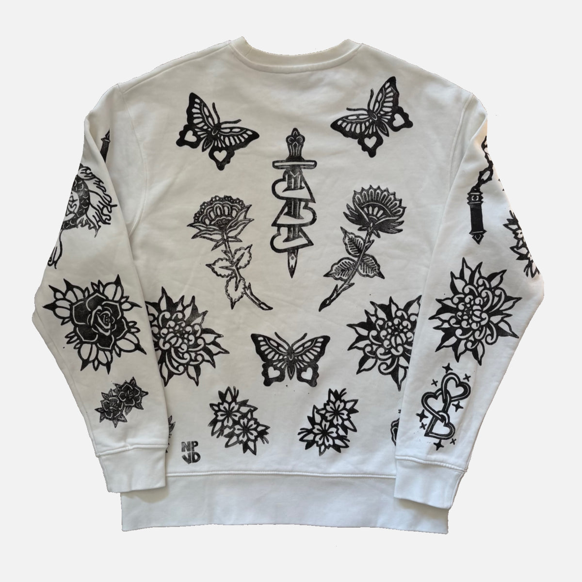 An off-white crewneck sweatshirt featuring black graphic prints of butterflies, roses, and a dagger, laid flat against a light gray background.