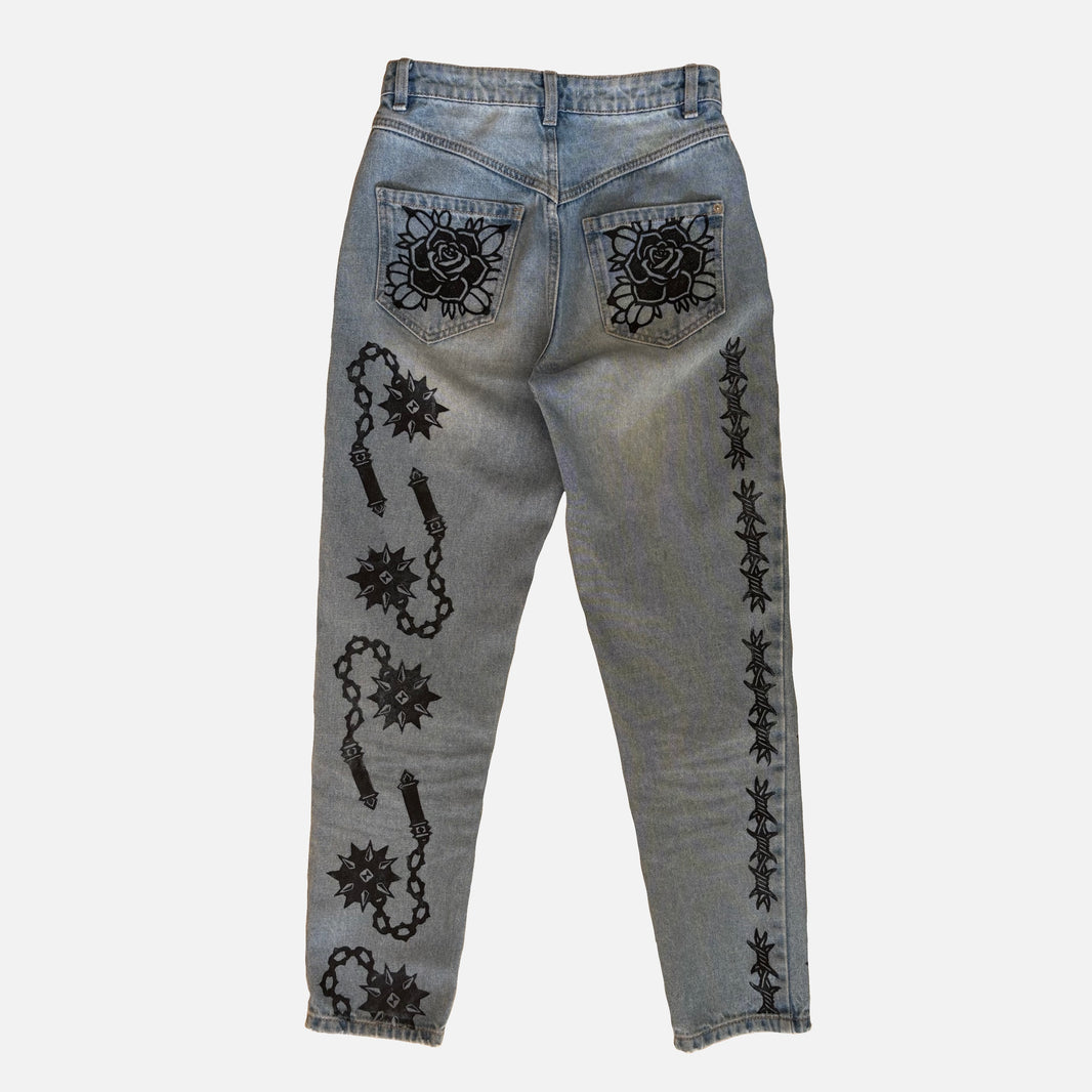 Light-wash blue denim jeans shown from the back, featuring black printed rose patterns on the back pockets and black chain-and-mace motifs down both legs.