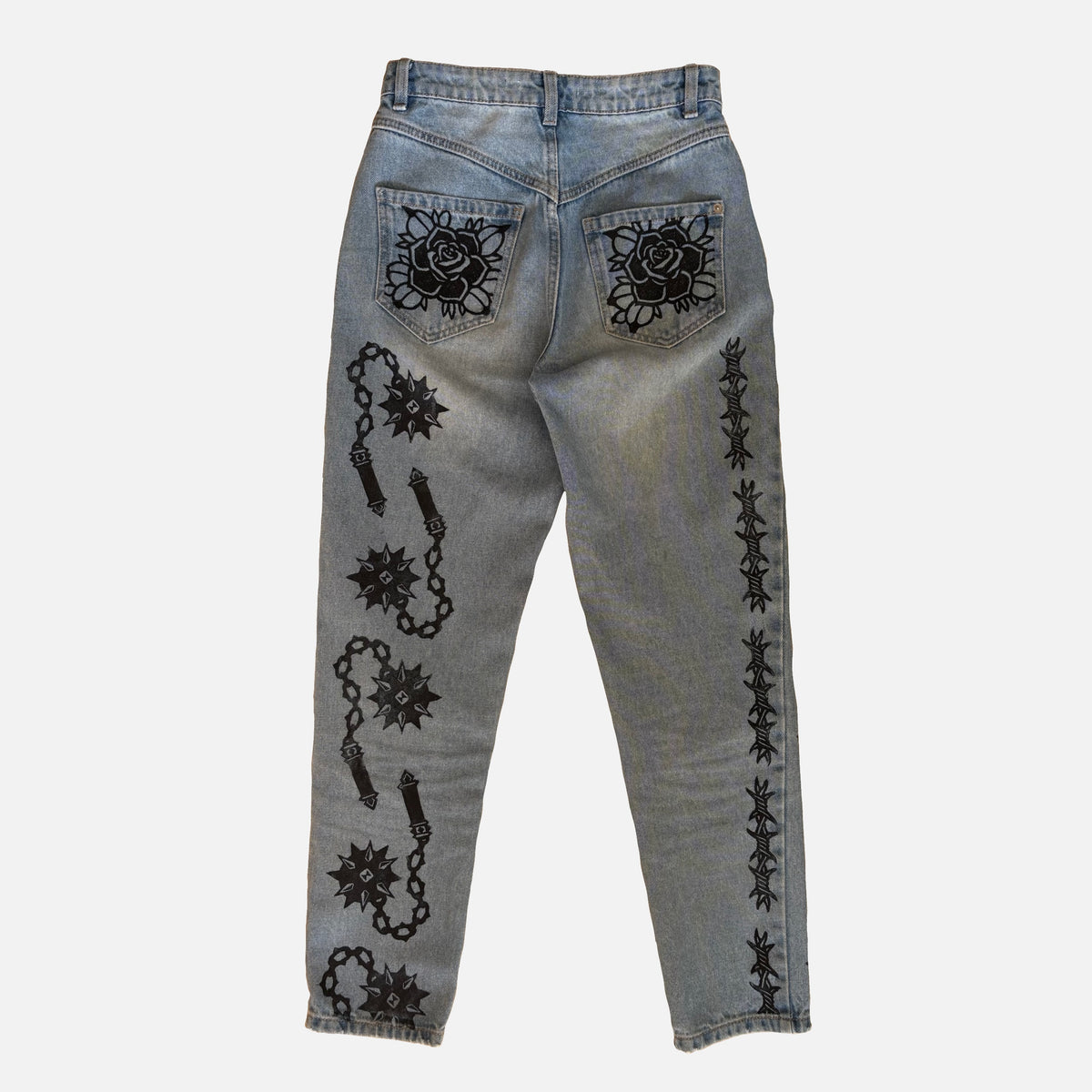 Light-wash blue denim jeans shown from the back, featuring black printed rose patterns on the back pockets and black chain-and-mace motifs down both legs.