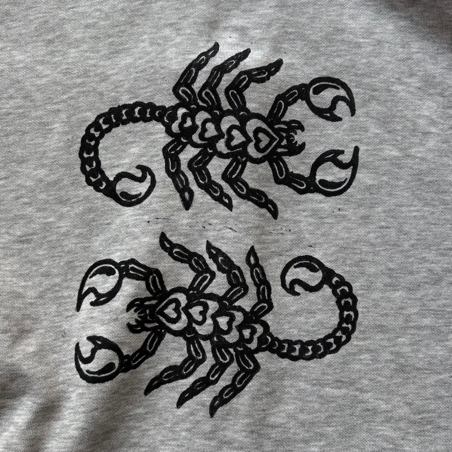 Close-up of a light gray heather fabric with black printed scorpion designs and a black barbed-wire motif along the top edge.