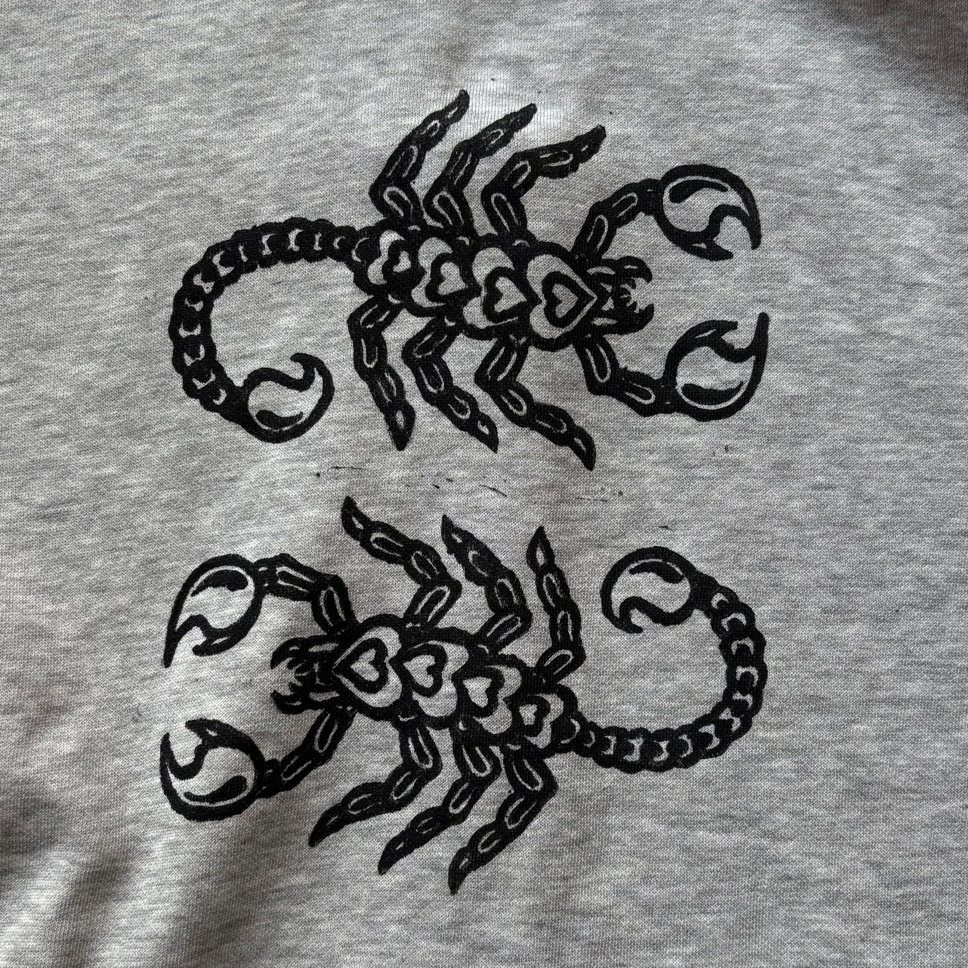 Close-up of a light gray heather fabric with black printed scorpion designs and a black barbed-wire motif along the top edge.