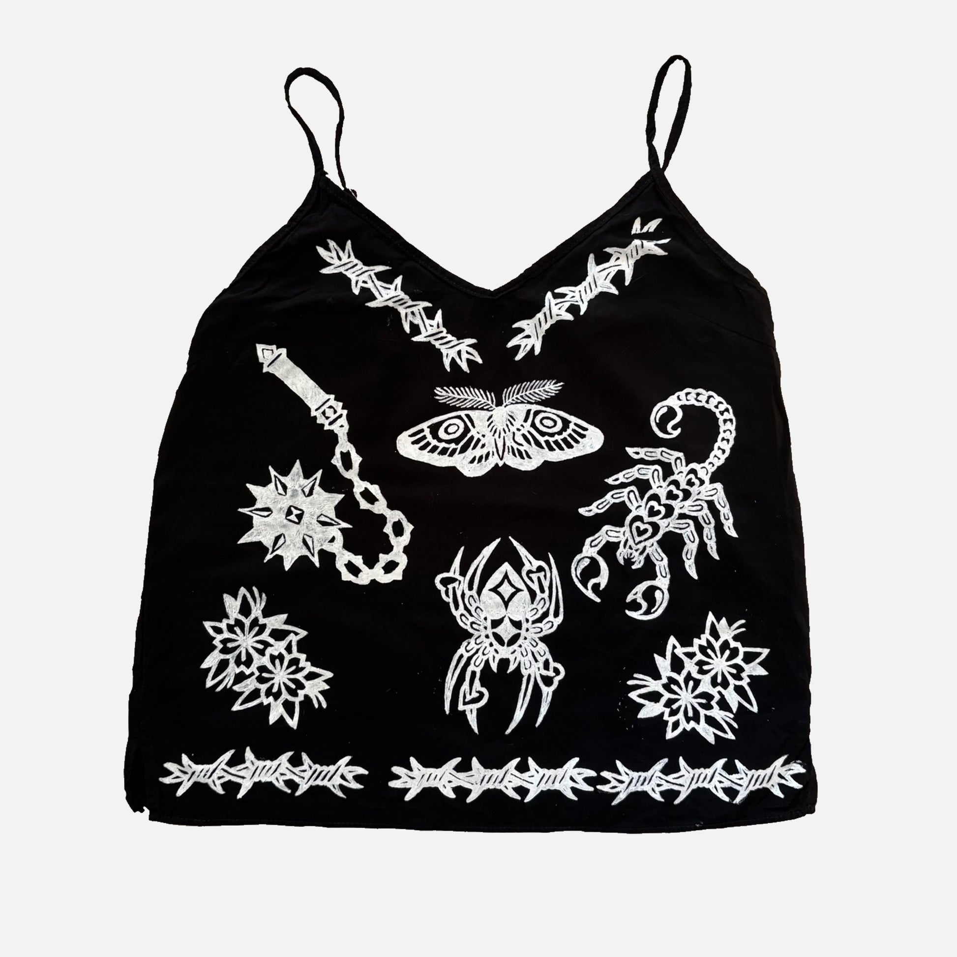 A black spaghetti-strap camisole top featuring white graphic prints of a scorpion, moth, dagger, and barbed wire borders, displayed against a light gray background.